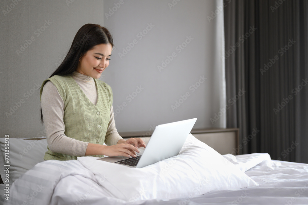 Beautiful asian woman in casual clothes working with laptop sitting on bed at home