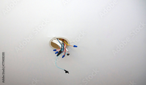 Exposed electrical wires protrude from a junction box in a ceiling, waiting to be connected to a fixture. The wires, secured with blue connectors, hint at ongoing electrical work