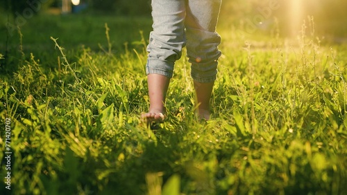 Children feet walk on green grass in summer, slow motion. Little bare legged kid girl, Healthy baby go in nature, active game. Boy go barefoot on green grass in park. Happy family, children happiness