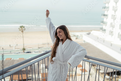 Chica joven en albornoz en balcón de un hotel sonriendo