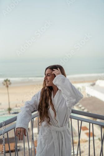 Chica joven en albornoz en balcón de un hotel sonriendo