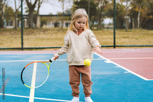 Child playing tennis on court outdoor, 4 years old kid girl training with racket and ball sport activity lesson healthy lifestyle