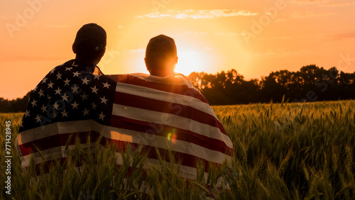 Two men with a usa flag on their shoulders look at the sunset photo