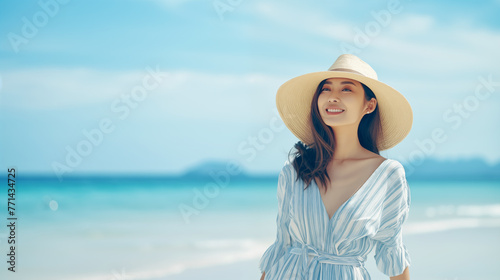 Oriental-looking girl in a hat and summer dress on a beach by the sea or ocean.
