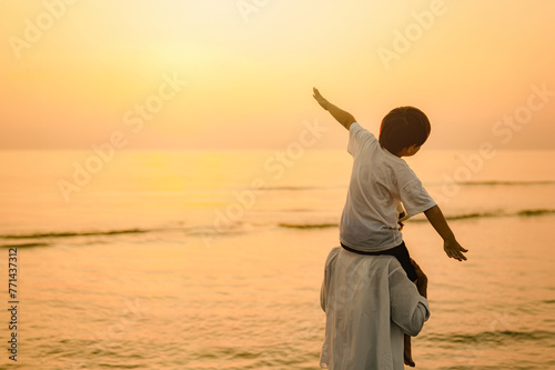 silhouette, sky, sand, sunlight, sea, beach, health, freedom, sunrise, sunshine. A young boy is standing on the beach with his father. The sky is orange and the water is calm.