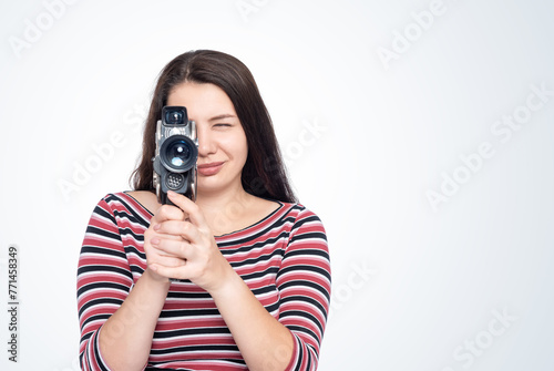 A happy young girl shoots a movie with an old film camera, front view, isolated on a light blue background