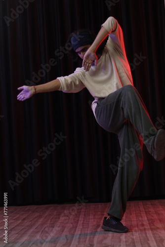 An Indian Modern Dancer Boy Wearing over sized full sleeves T-Shirt and loose lower pants, dancing and posing in front of black curtain, modern