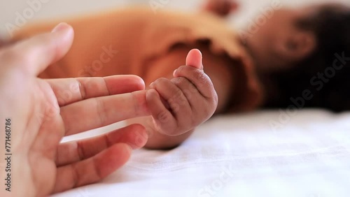 a white mother's hand strokes the small hand of an African-American baby on a white bed, a close-up of the hands of a Caucasian mother and a black baby