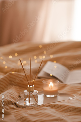 Liquid home perfume in glass bottle with bamboo sticks on ceramic tray in bed over glowing lights. Cozy atmosphere. © morrowlight