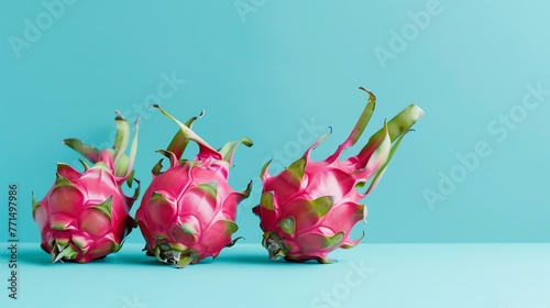 Three ripe dragon fruits on a blue background. The fruits are pink and have green leaves. The background is a light blue color. photo