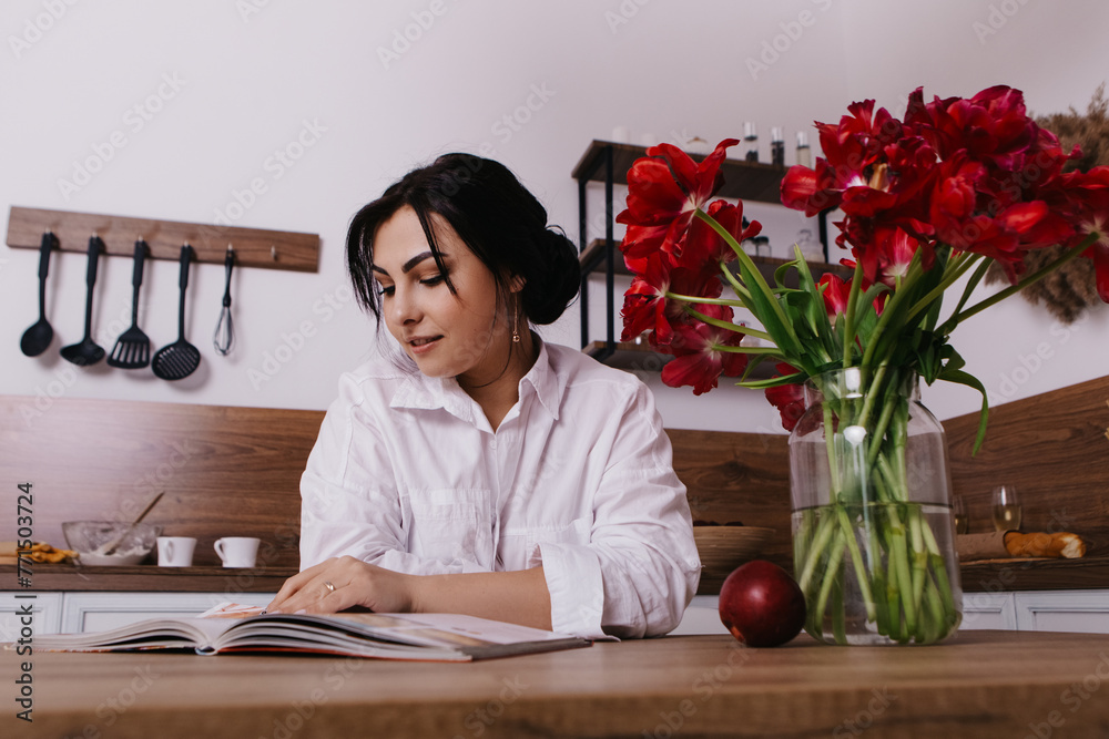 Woman poses with vibrant bouquets of red tulips in vase in kitchen, look and read recipe book. Spring International Women`s Day, 8th of March. Holiday, festive, celebration
Woman poses with vibrant bouquets of red tulips in vase in kitchen, look and read recipe book. Spring International Women`s Day, 8th of March. Holiday, festive, celebration