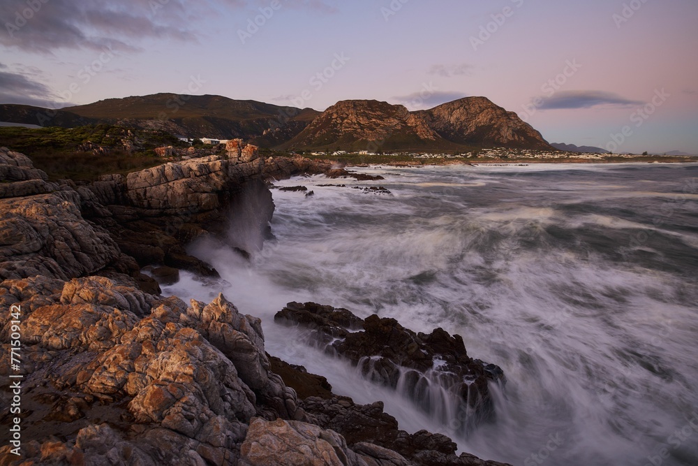 Beautiful sunset over a rocky coast, with waves crashing against the shore. Hermanus, Western Cape.