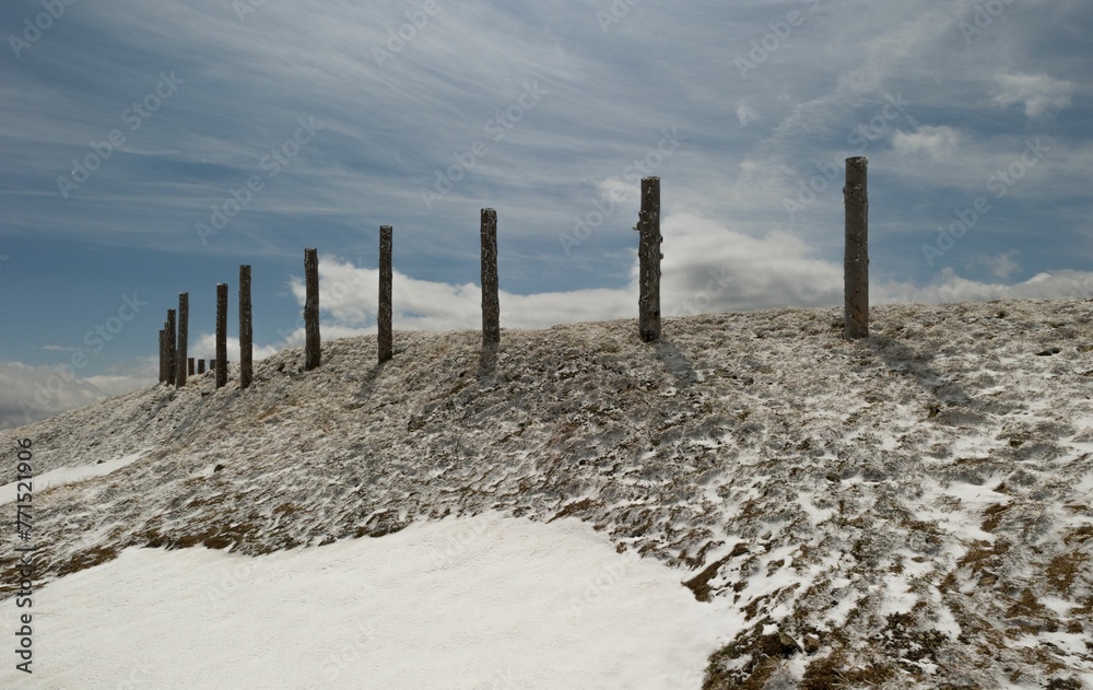 Wooden fence atop a snow-covered hill, with a white, snowy slope below