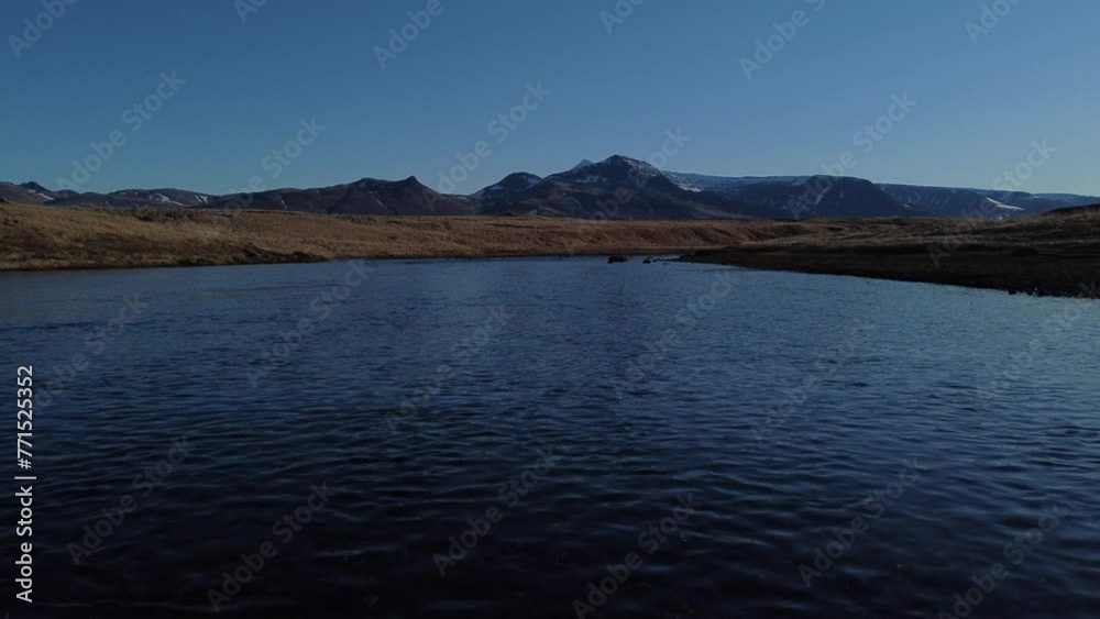 Aerial of a calm lake with mountains in the background against the blue sky Aerial of a calm lake with mountains in the background against the blue sky
