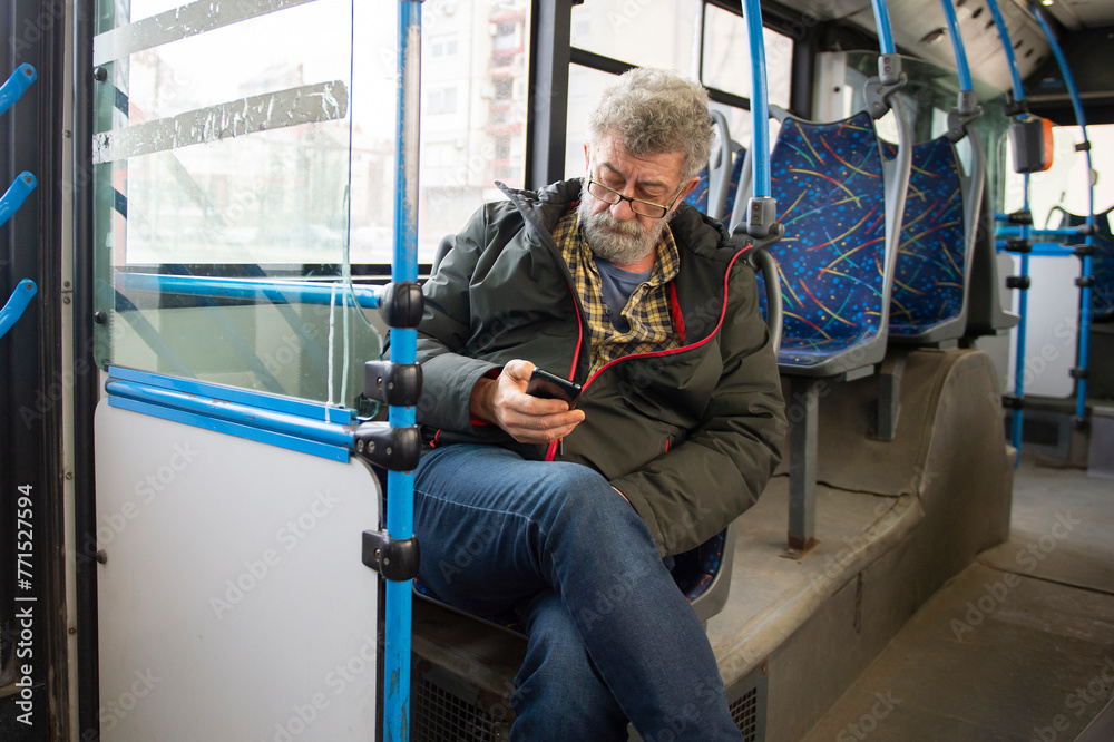 A man is sitting on a seat while riding a bus and having fun with his phone A man is sitting on a seat while riding a bus and having fun with his phone