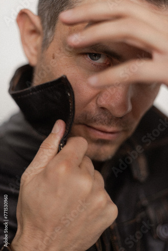 a man in a leather jacket looks through his fingers