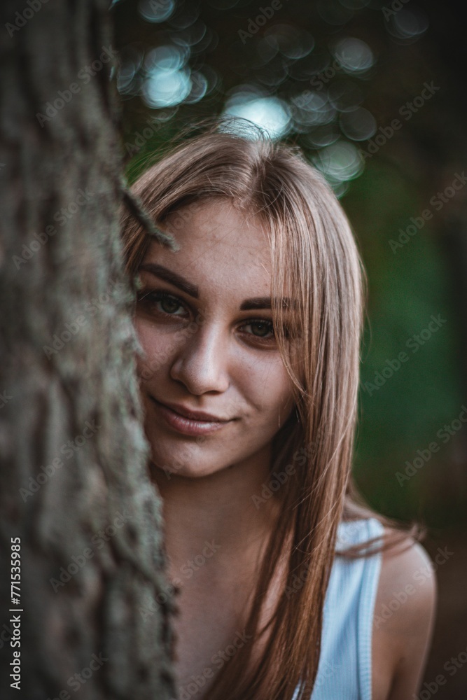 a young woman smiles while leaning on a tree trunk in the forest a young woman smiles while leaning on a tree trunk in the forest