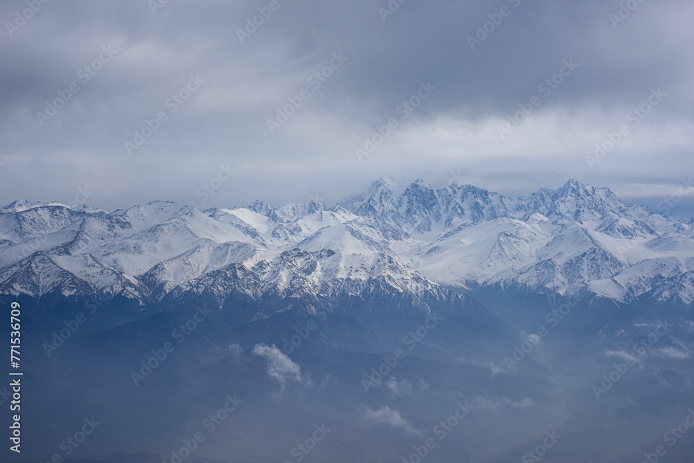 Aerial view of the snow-capped Ten-Zan Bodga peak with clouds floating above it
