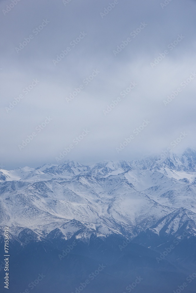 Obraz premium Vertical view of the snow-capped Ten-Zan Bodga peak with clouds floating above it