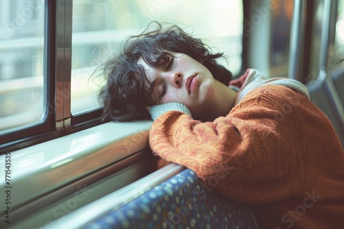 A young person with curly hair rests their head against a train window, succumbing to sleep in a cozy sweater. Generative AI photo