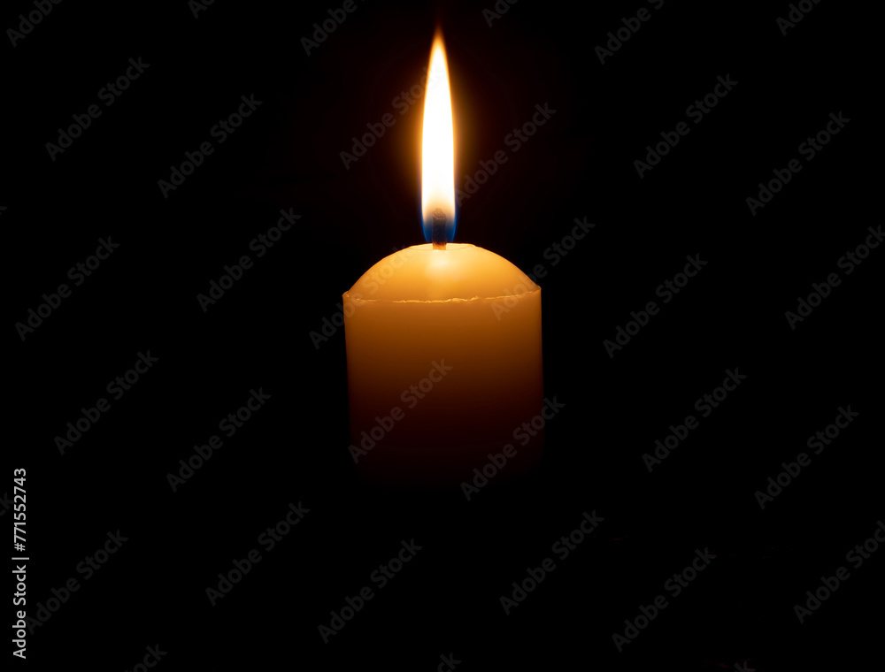 Single burning candle flame or light glowing on big white candle on black or dark background on table in church for Christmas, funeral or memorial service with copy space Single burning candle flame or light glowing on big white candle on black or dark background on table in church for Christmas, funeral or memorial service with copy space
