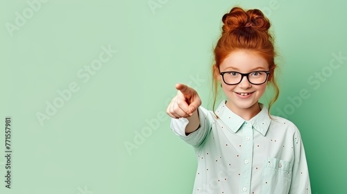 red-haired smiling girl schoolgirl points her finger to the side on a green background  space for text