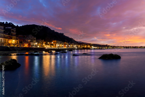 evening or night landscape of evening town coastline in golden lights and sea gulf with calm water and nice reflections with beautisul sunset sky on background