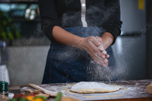 A woman stands in the kitchen and uses her hands to rub flour. which is the process of making pizza to food concepts and homemade pizza photo