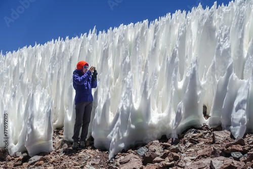 
A woman in the Atacama Desert, Chile, captures the towering penitentes with her camera. The ice formations, taller than herself, create a unique and surreal landscape.  photo