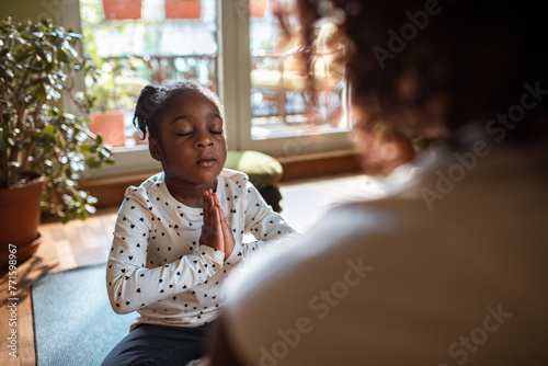 Young mother teaching her daughter how to do yoga and meditate at home photo