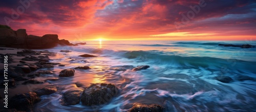 As the sun sets, casting a warm afterglow over the rocky beach, waves crash against the rocks under a sky filled with cumulus clouds