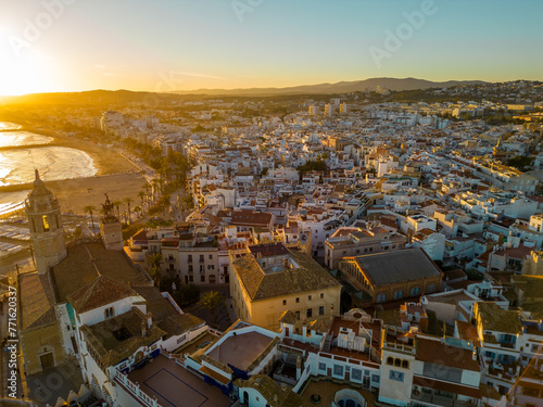 Aerial view of Sitges City at sunset. Orange sunset, sun in front of the camera. Travel destination. Beautiful warm colours at sunset, reflecting on buildings and in water. Sunset Point. 