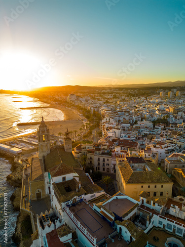 Aerial view of Sitges City at sunset. Orange sunset, sun in front of the camera. Travel destination. Beautiful warm colours at sunset, reflecting on buildings and in water. Sunset Point. Vertical 