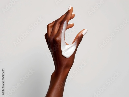 Elegant dark-skinned hand with a dollop of cream on the back, against a light background, conveying skincare beauty photo