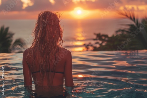 The back view of a woman in a pool as she gazes at the captivating sunset over the ocean horizon