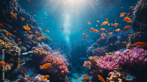 A colorful coral reef with many fish swimming around. The fish are orange and the water is blue © Rattanathip