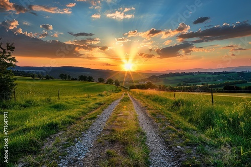 A dirt road runs through a vibrant green field under a dramatic sunset, creating a striking contrast