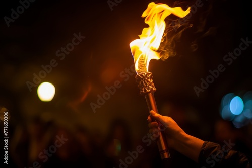 An individual holds a stick with blazing flames during a nighttime event, symbolizing unity, strength, and ignition