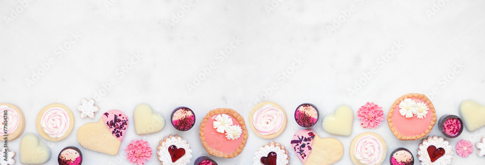 Obraz premium Mothers Day or love themed baking bottom border with a selection of cookies and sweet treats. Top down view on a white marble banner background with copy space.
