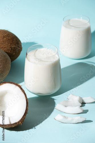 Coconut milk in a glass among coconuts on a blue background