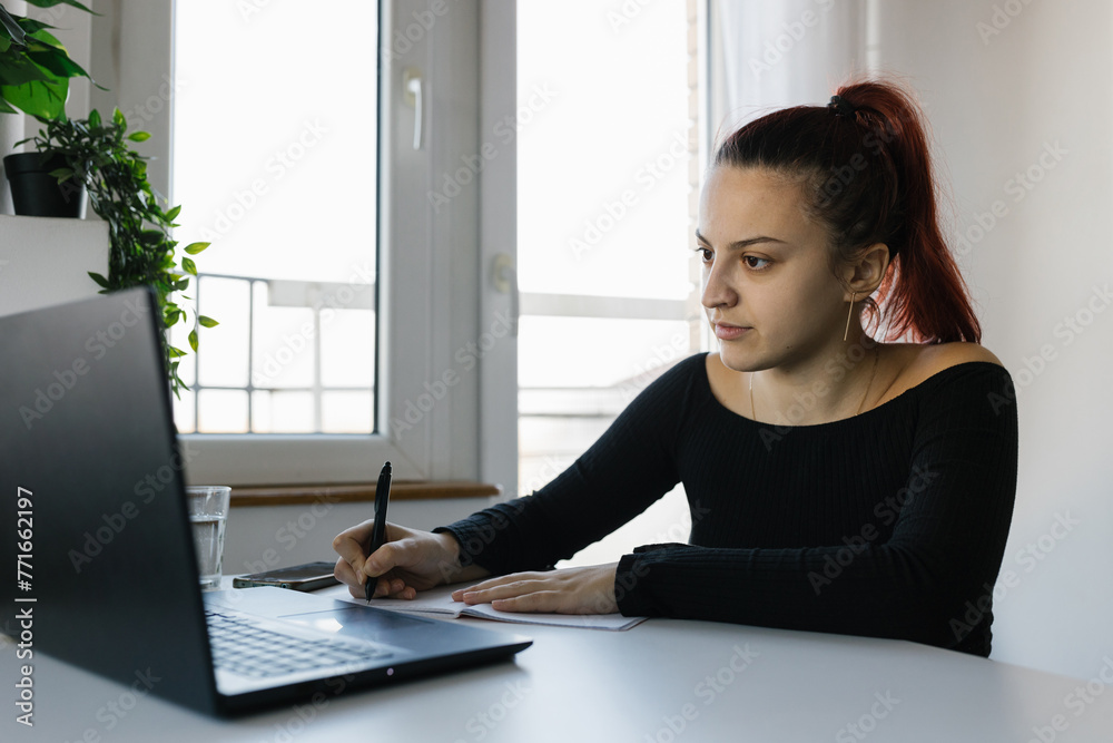 Obraz premium Young female student using laptop and notebook, studying at home 