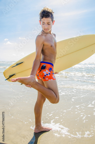 Photography Teenage male surfer stops to check the bottom of his foot while carrying his sur