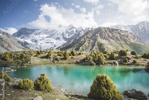 Panorama of mountain ranges and turquoise cold mountain lake on a warm sunny evening in the Fan Mountains in Tajikistan, Tien Shan highlands in the evening