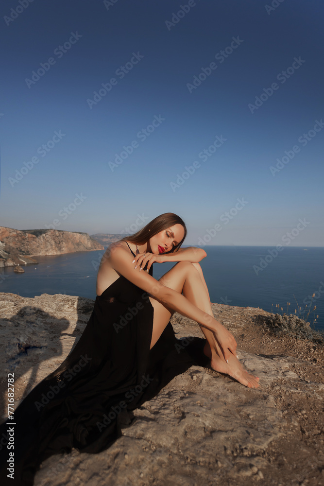 woman in black dress stands looking into the sea on a rock