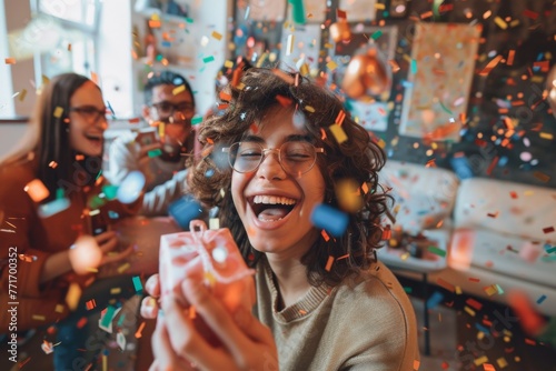 Excited young woman laughing and holding a gift surrounded by flying confetti photo