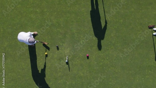 Playing croquet. Aerial view of a player in a croquet course in green lawn, slow motion, preparing and hitting the ball  (Drone shot, 4K ) 