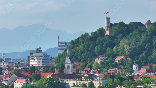 AERIAL COPY SPACE: Ancient castle atop the verdant hill overlooks the sunlit cityscape. Cinematic drone point of view of the old Ljubljana downtown on a sunny day in spring. Castle above European city photo