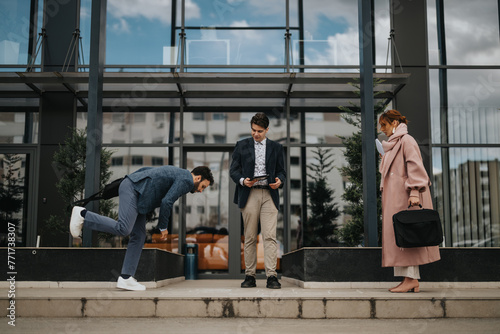 Young male business person stumbling while walking on a sidewalk, his colleagues are looking at him.