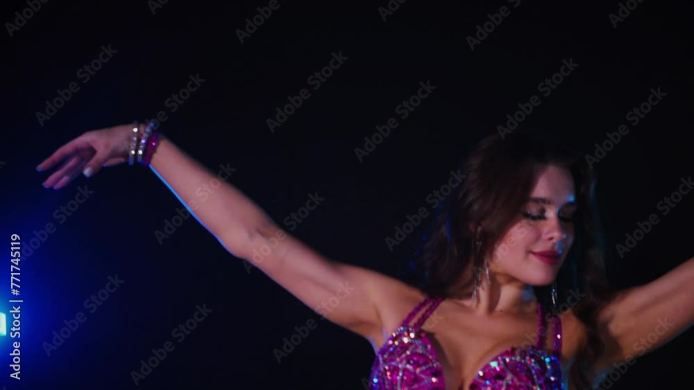 Woman in purple dress gracefully dancing belly dance in dimly lit room. Slow motion shooting. Elegantly dressed woman moving to music and dancing oriental dances in dark setting. Female dancer wearing Woman in purple dress gracefully dancing belly dance in dimly lit room. Slow motion shooting. Elegantly dressed woman moving to music and dancing oriental dances in dark setting. Female dancer wearing