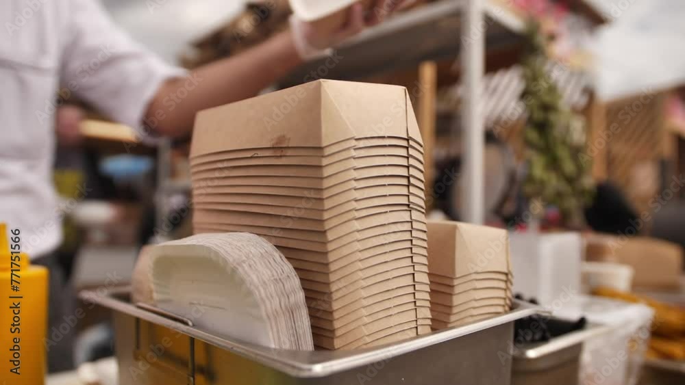 A man distributes orders to customers in cardboard boxes for food delivery. A restaurant employee is collecting a takeaway food box. 